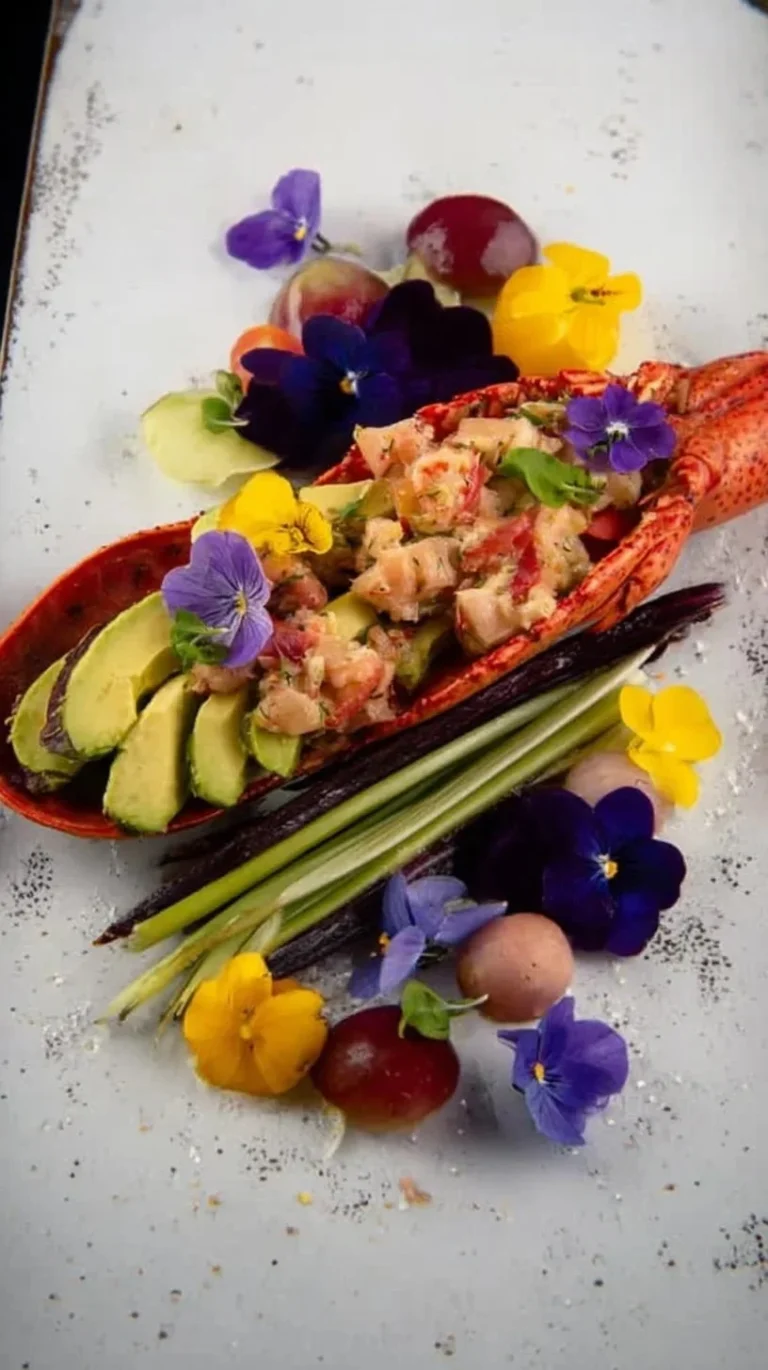 Plat de homard breton avec avocat, légumes croquants et fleurs de pensée
